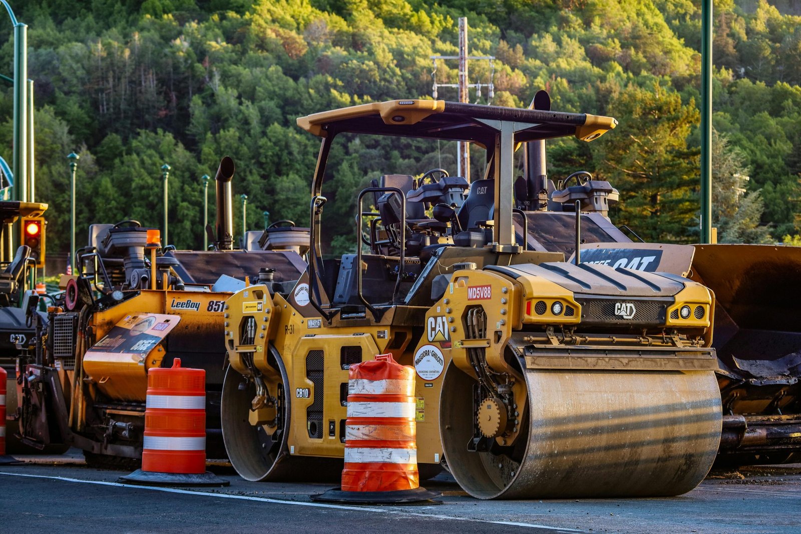Construction machinery and vehicles on site with road rollers and cones.